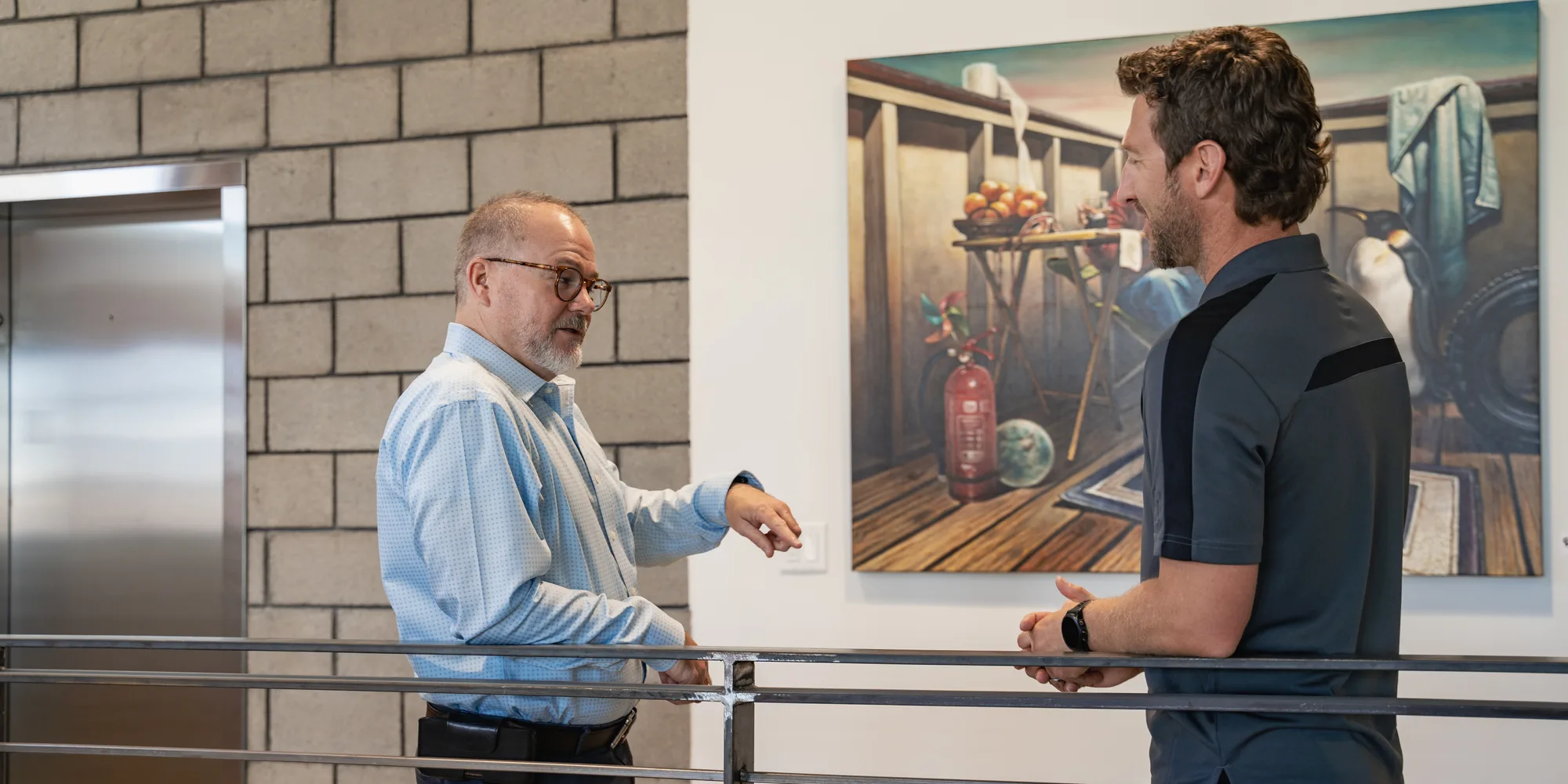 Two people talking beside a painting in an office hallway