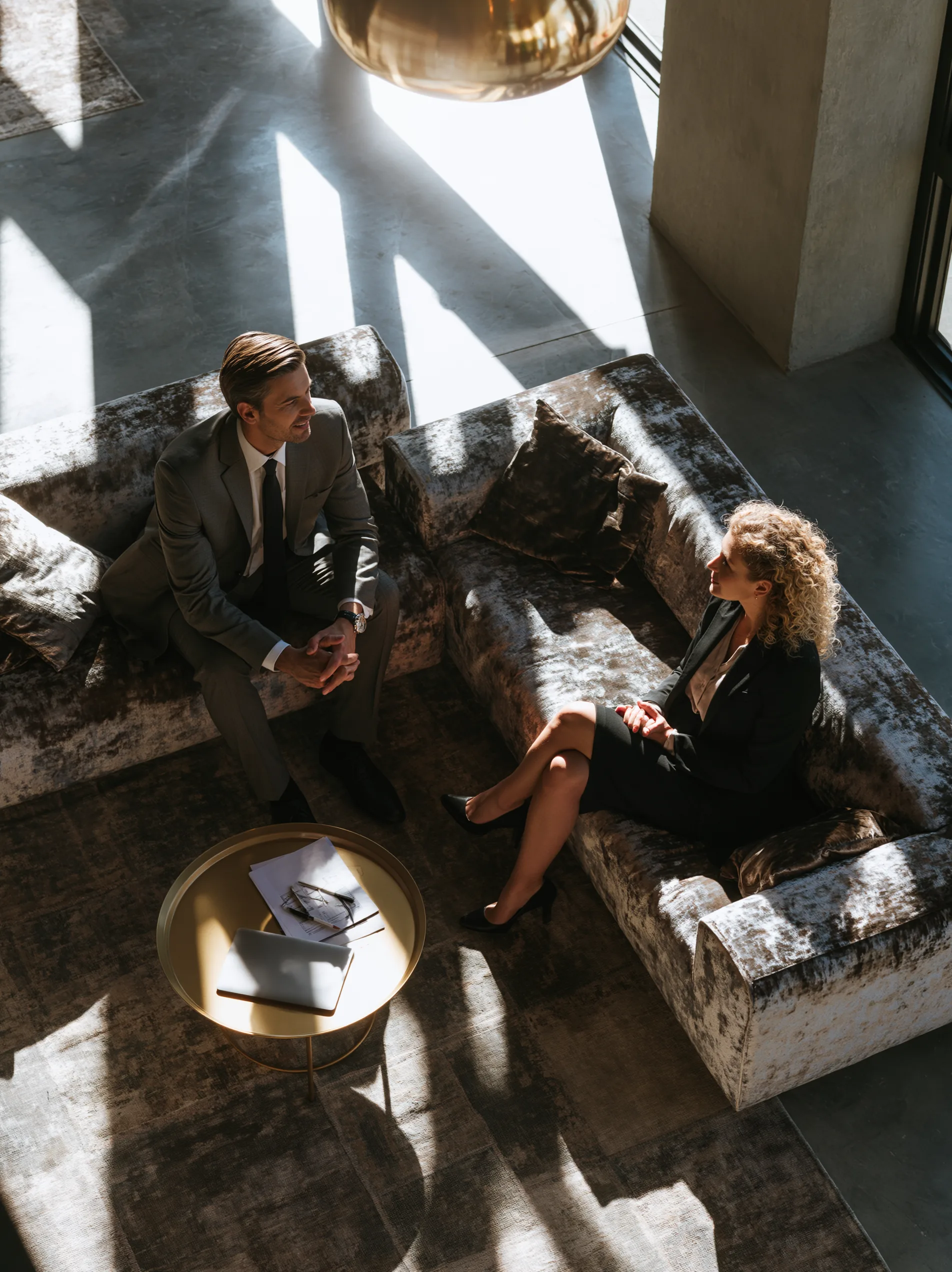 Two people in conversation across a low table in a daylit lounge