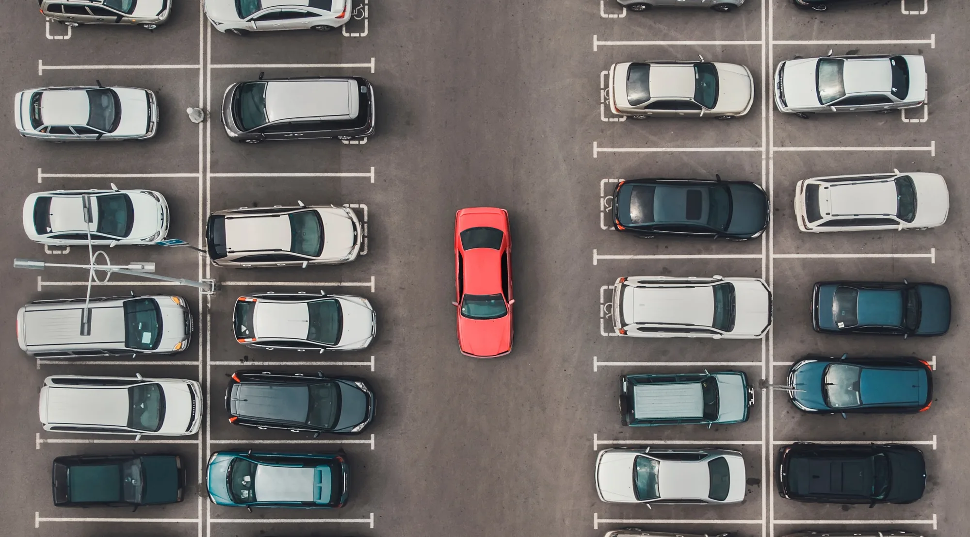 An overhead view of a parking lot with one red car among grey ones